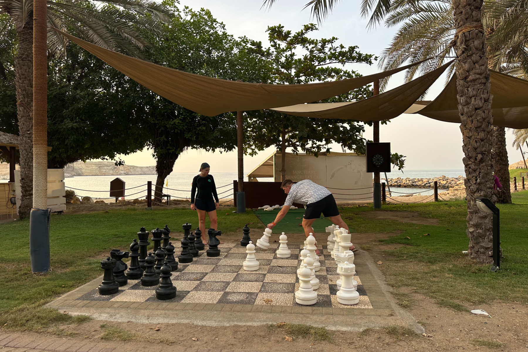 My husband and daughter playing giant chess with the beach behind them