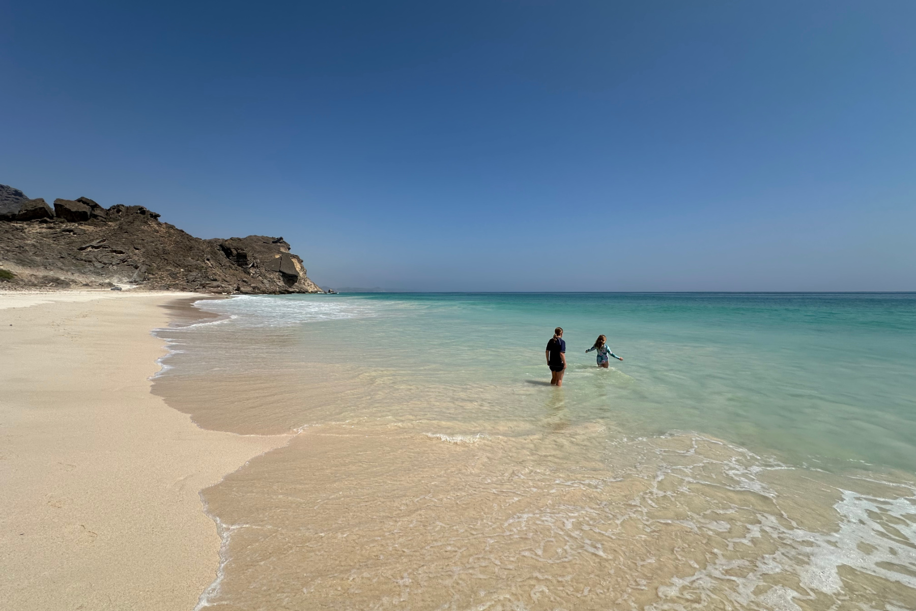 my daughters stepping into the turquoise sea at Fazayah Beach