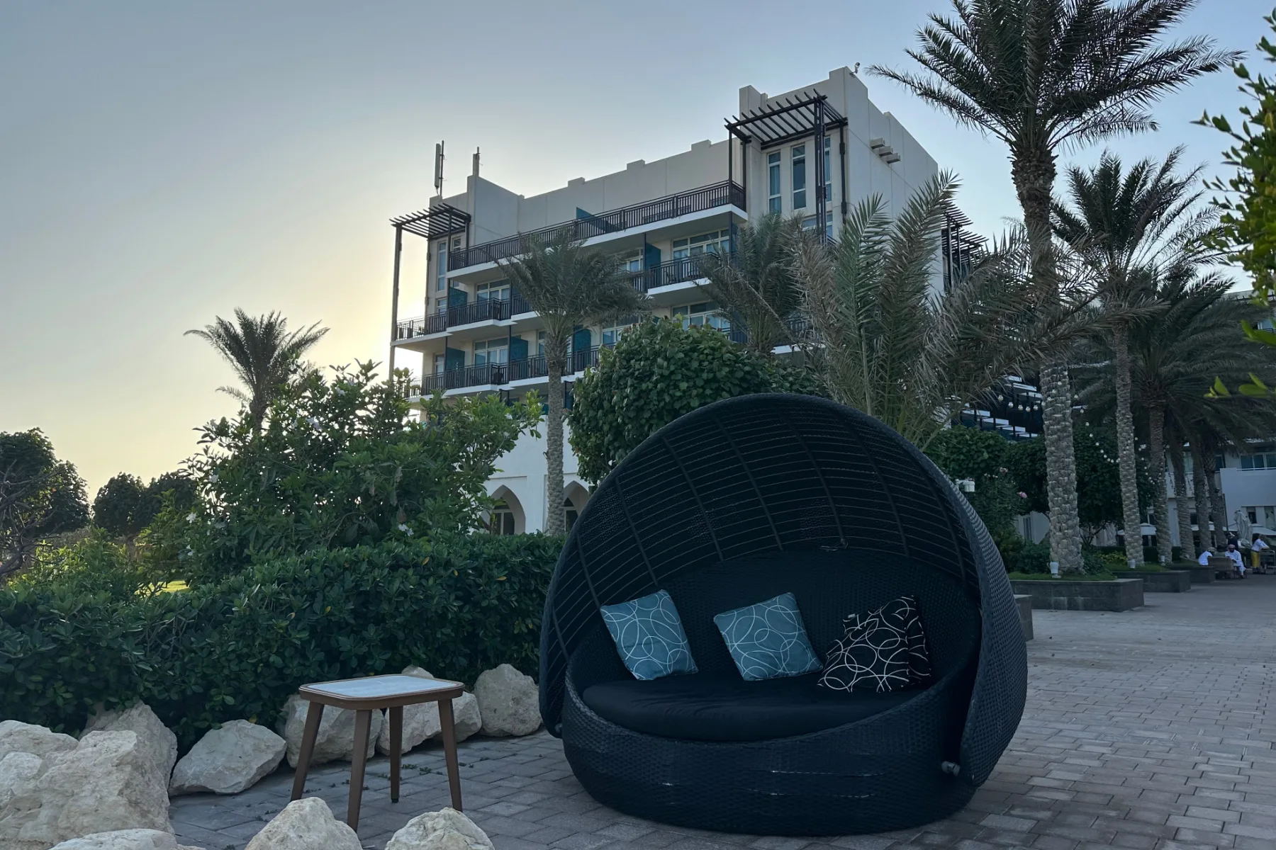 A large bucket chair outside the back of the Crowne Plaza Duqm hotel. Behind it there is a view of the executive suite wing of the hotel. The sun is setting