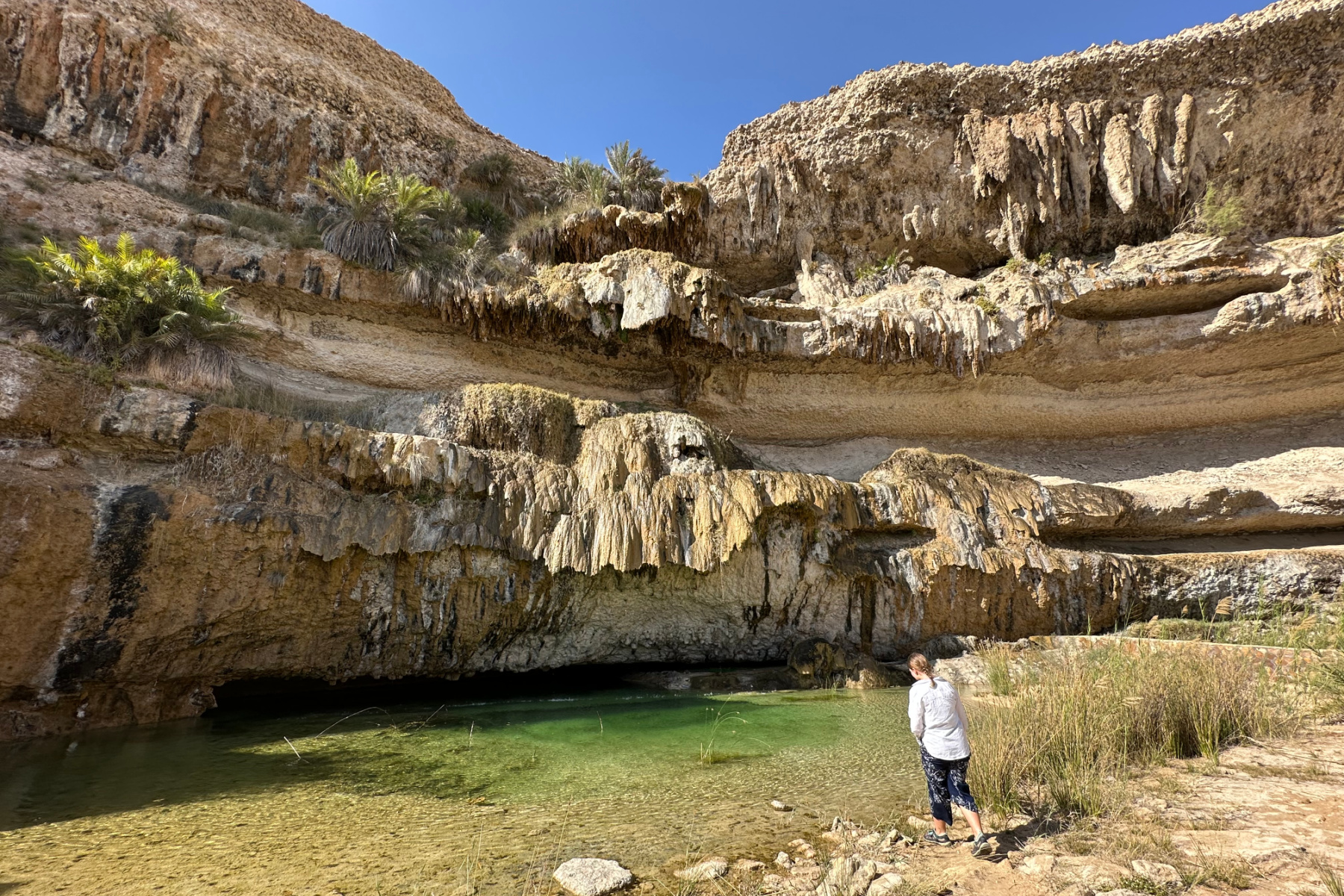 My daughter standing on the edge of the water pool below the falls in Wadi Shuwaymiyyah