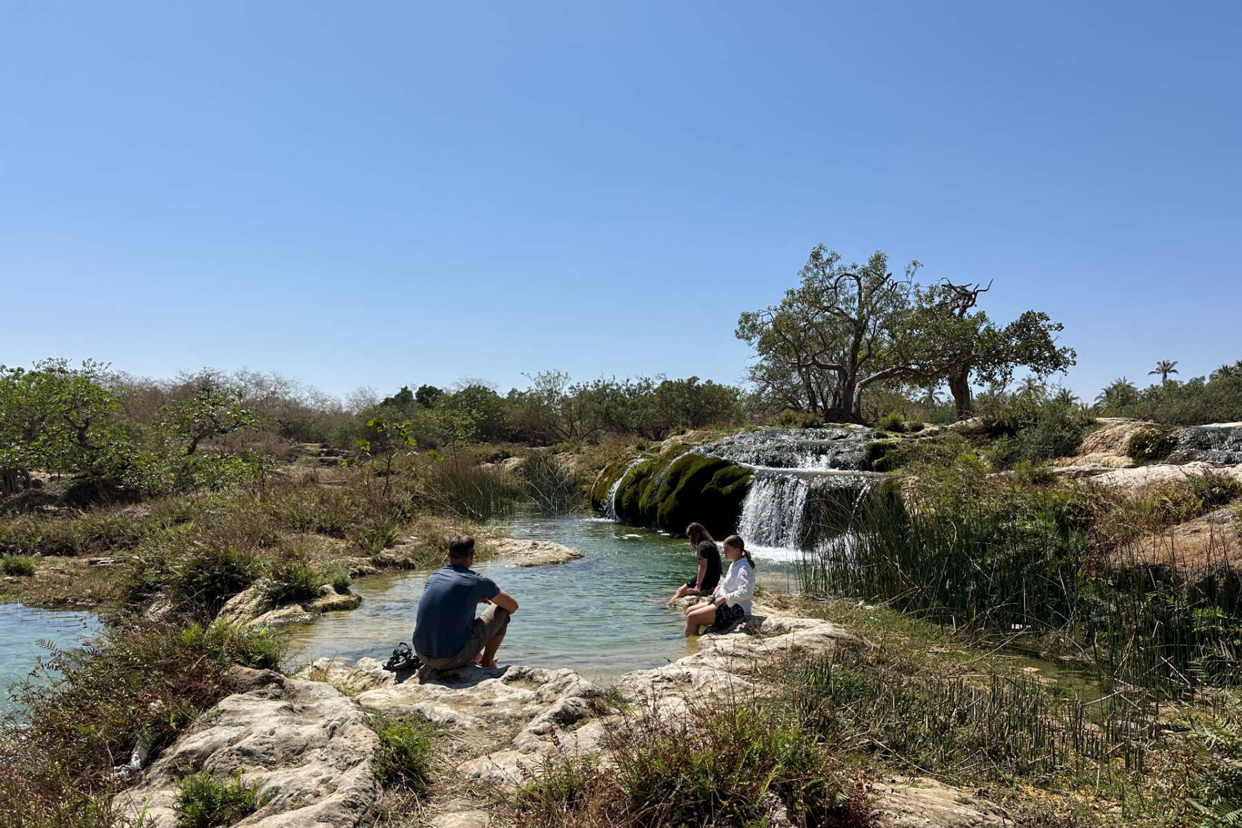My family sat beside a pool of water at the Wadi Darbat Step Waterfalls