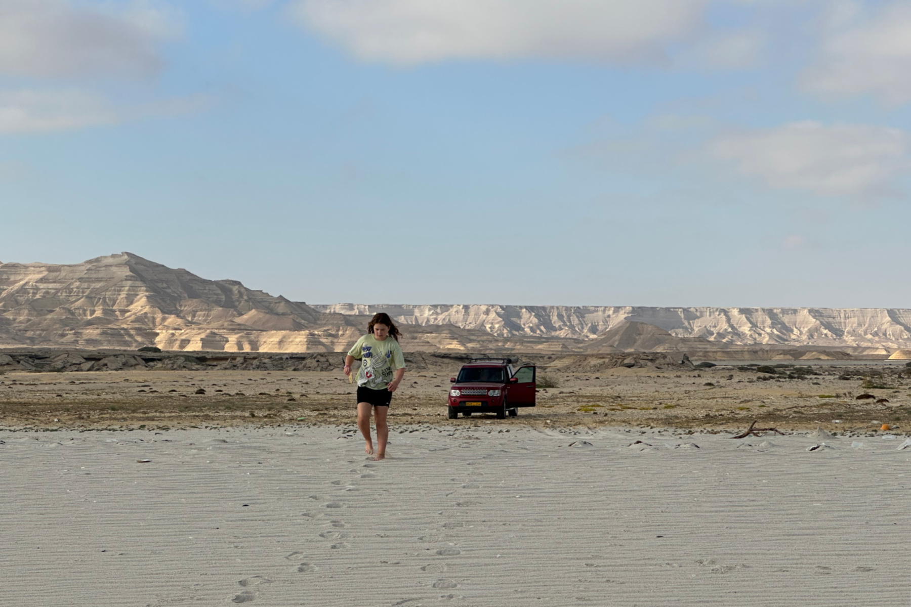 Our daughter walking on the beach at Shuwaymiyyah. Our car is parked on the sand behind her and in the distance there are mountains