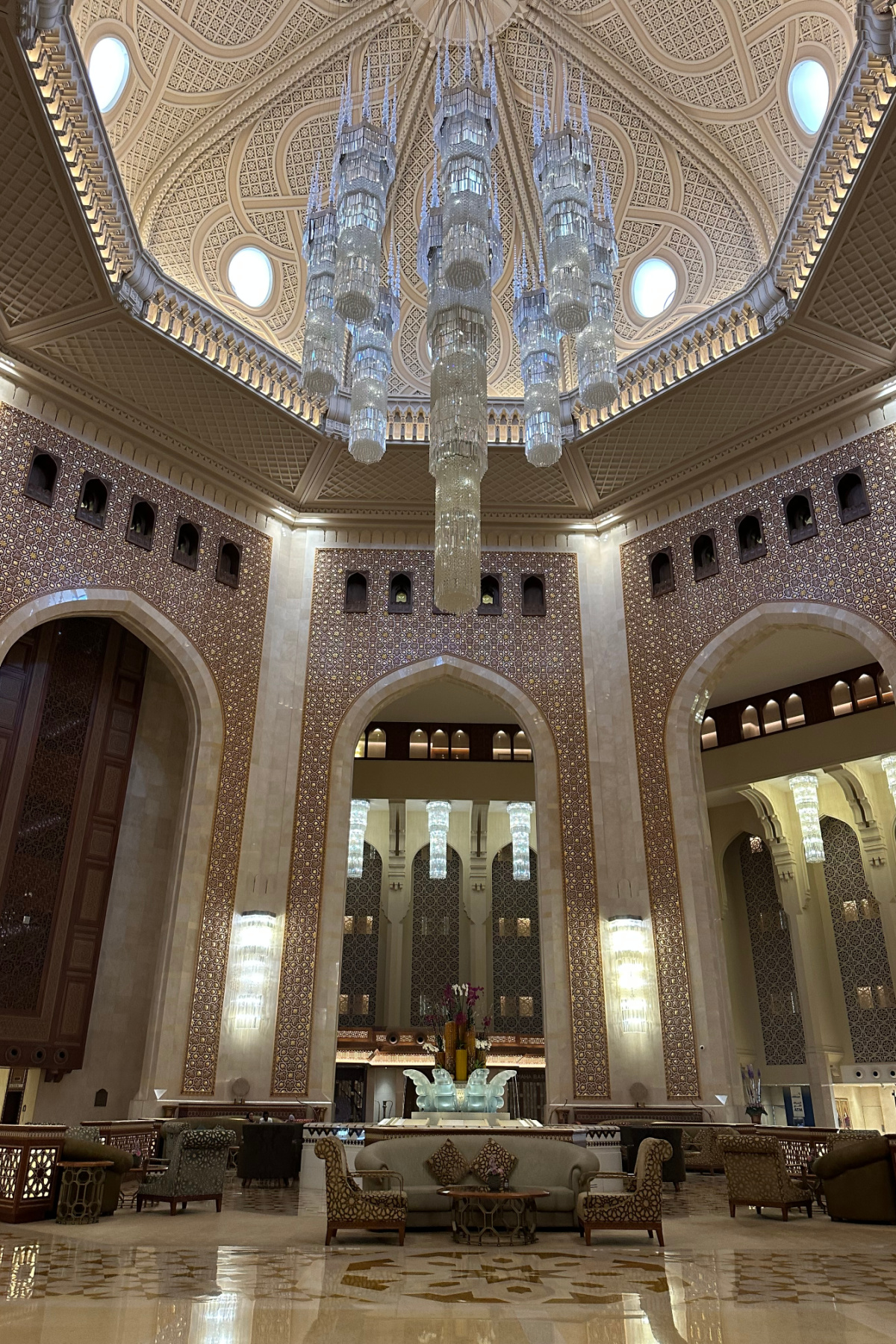 The crystal chandelier in the hotel lobby. The walls are covered in Arabic tiles, the floor is marble and the furniture looks like it has been designed for royalty