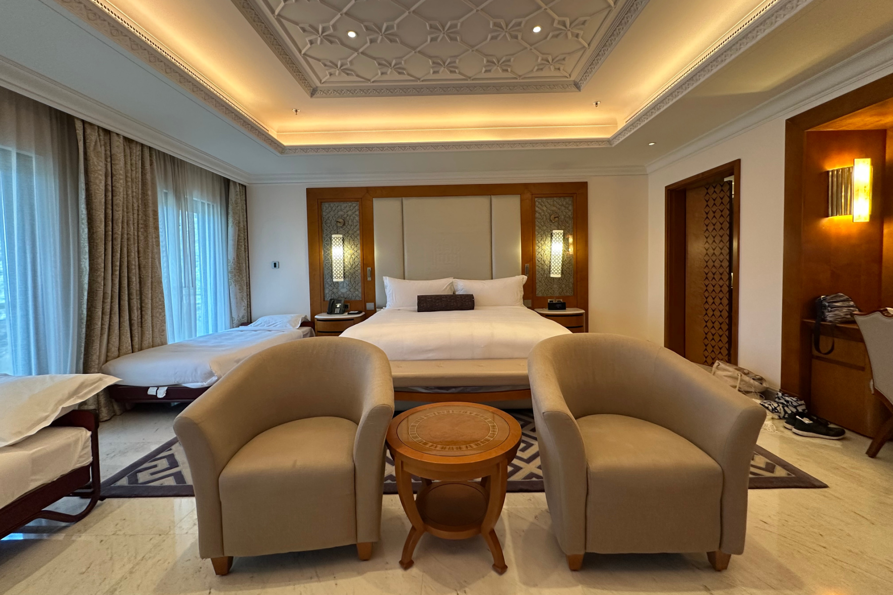 The master bedroom in the Sohar Presidential Suite. There are two bucket chairs at the end of the bed and light decor accented with Arabic designs