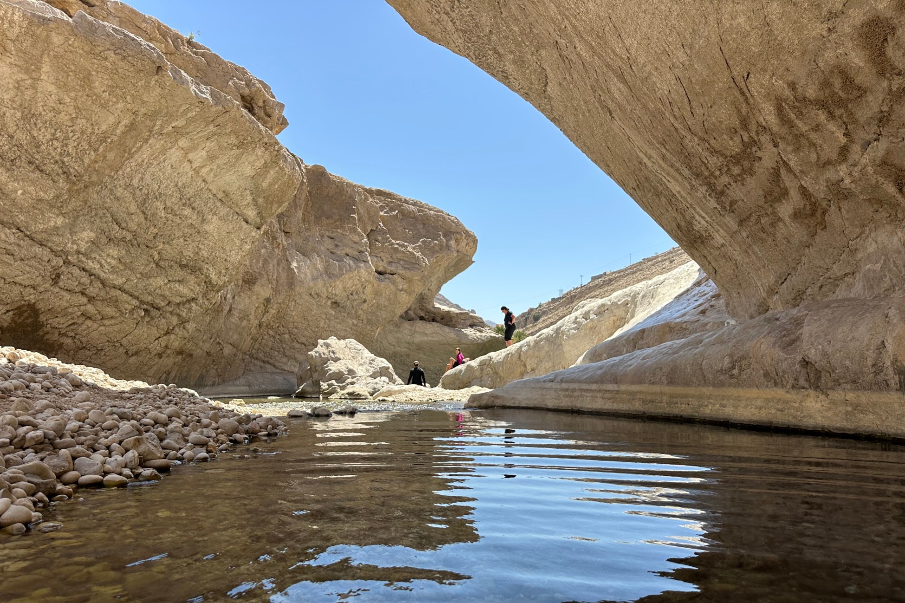 A limestone overhang in Wadi Bani Khalid. Mu family and friends are cooling off in the water in the distance.