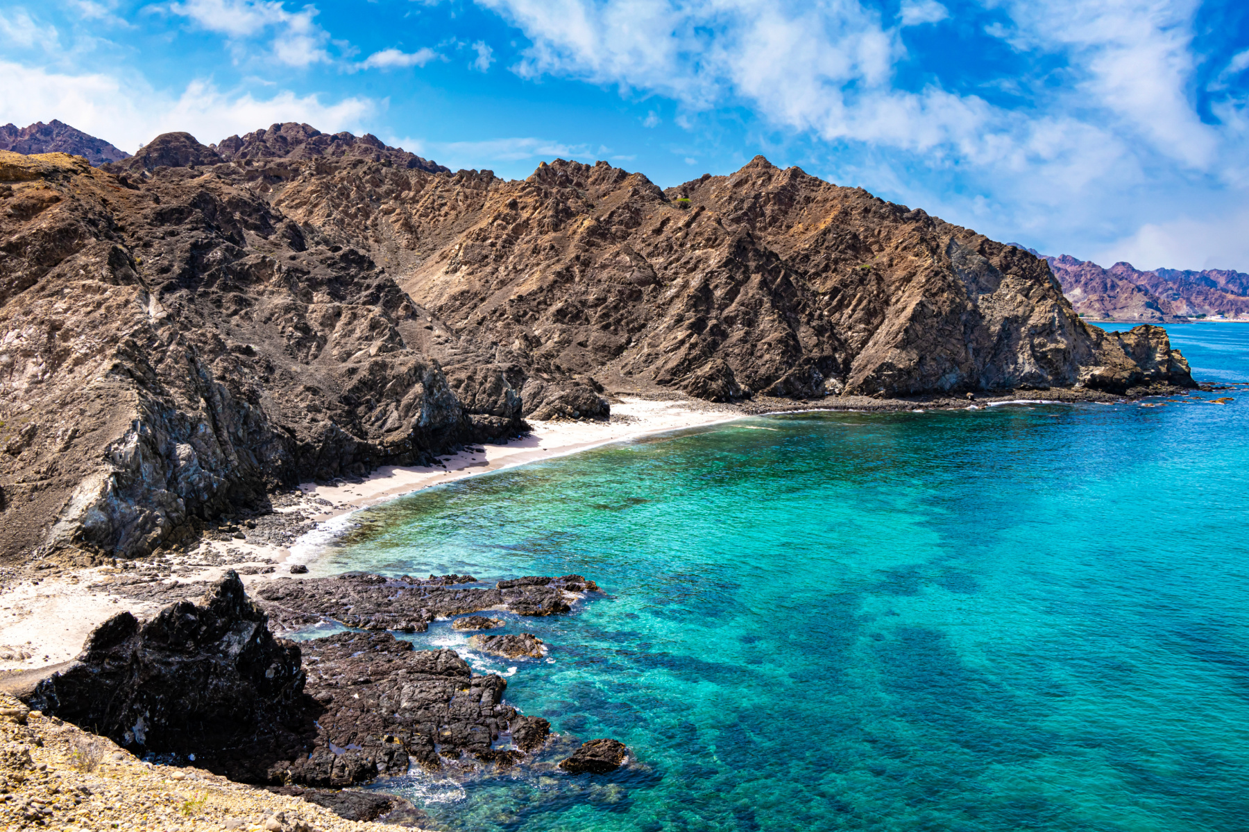 A view across the turquoise water which meets the beach and mountains at Qantab in Muscat, Oman