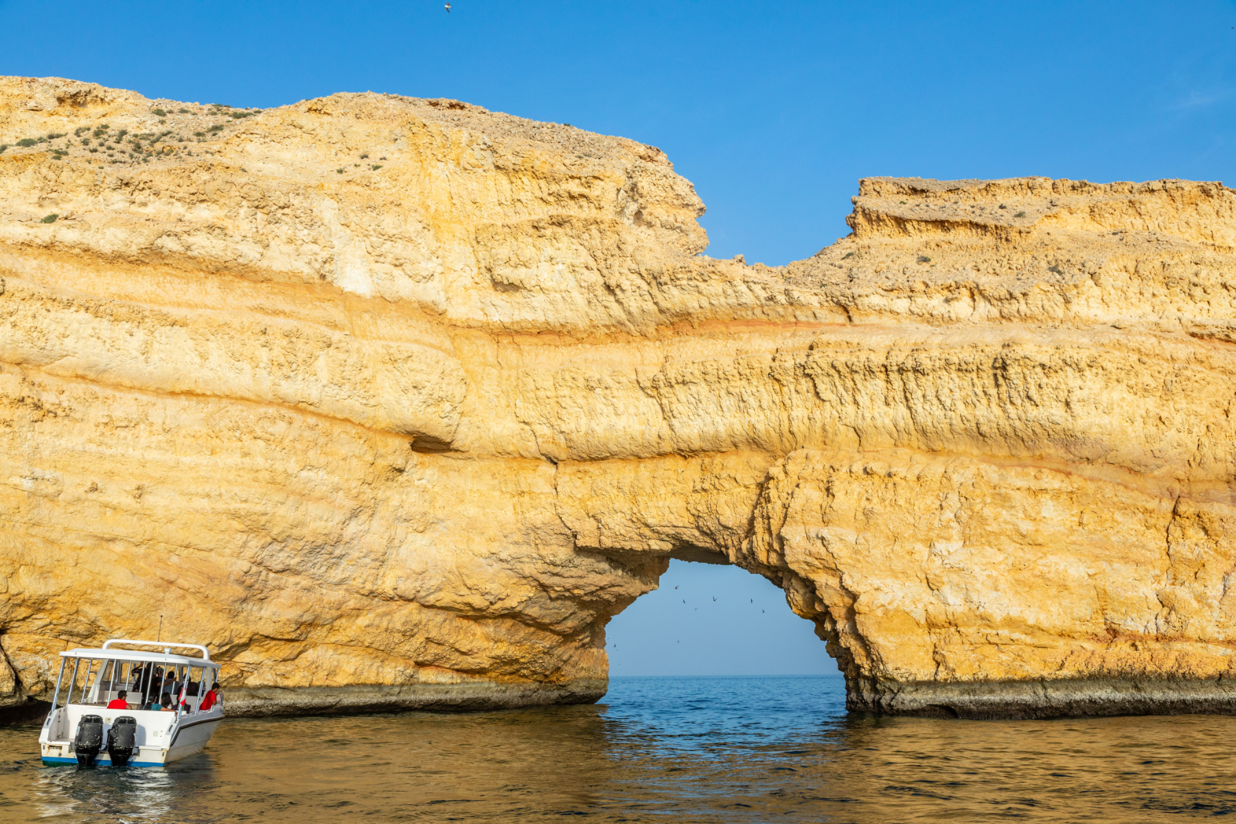 Qantab natural arch passage in the rock and boat full of tourists, Muscat, sultanate Oman
