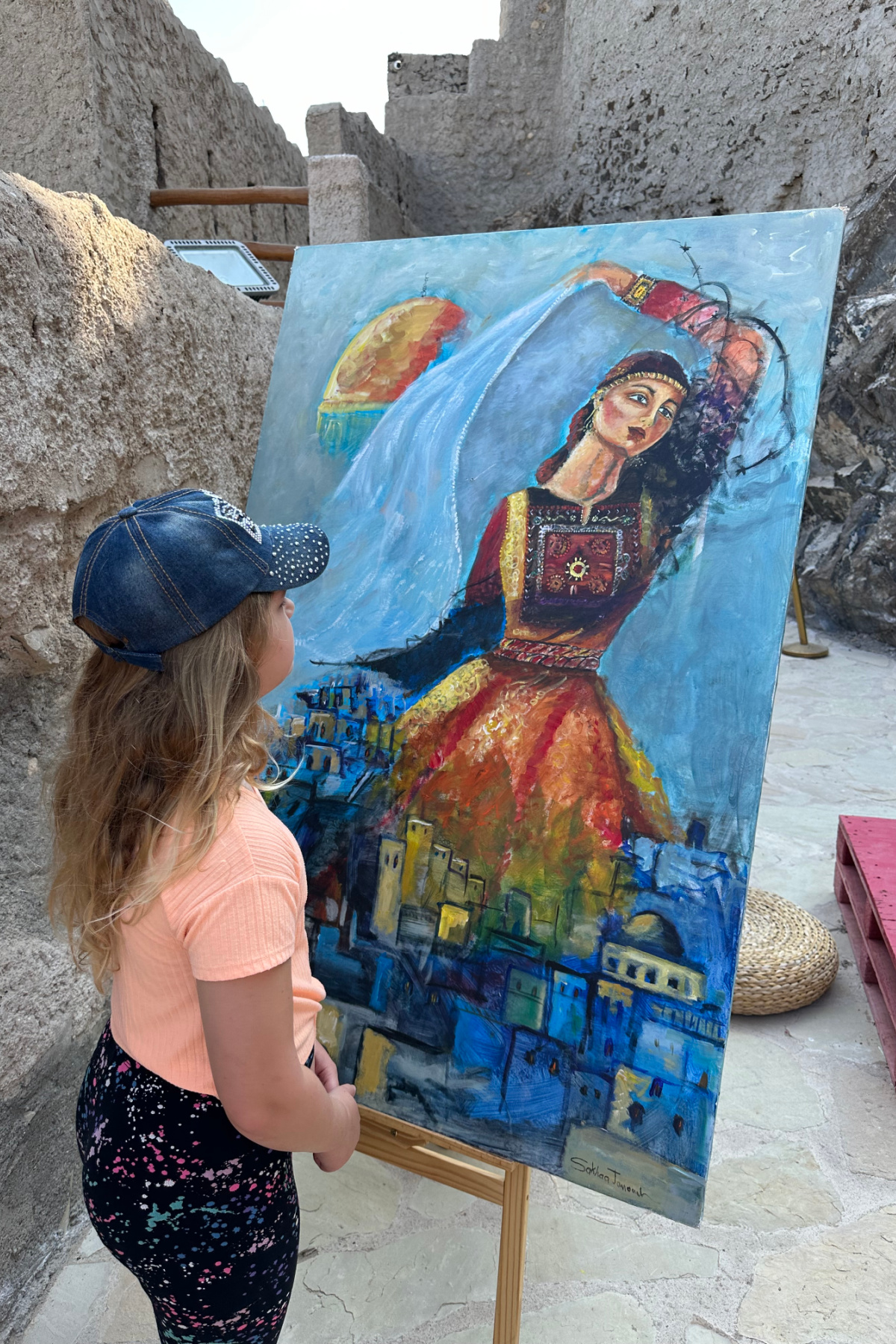 My daughter looking at a painting of a dancing woman on display on the battlements of Muttrah Fort in Muscat