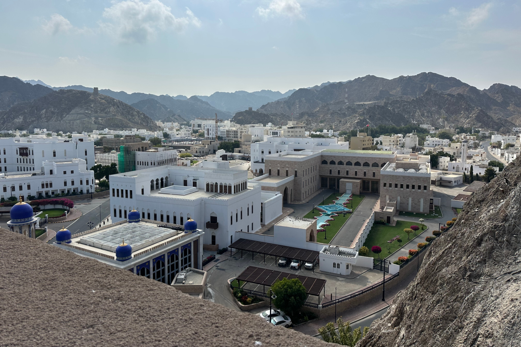 A view over the sand coloured battlements of Al Mirani Fort towards the white buildings oand formal gardens of the Omani and French Museum in Old Muscat