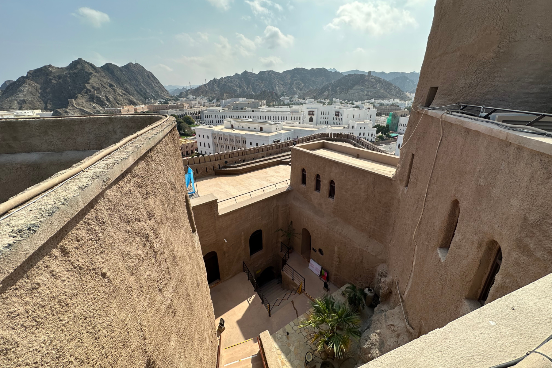 A view over the snad coloured walls and interior of Al Mirani Fort towards the white government buildings of the ministries district in Old Muscat